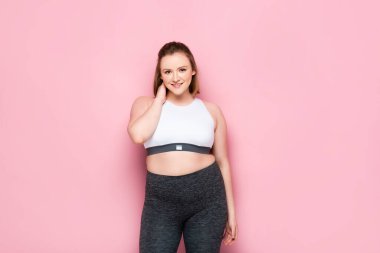 Çekici şişman kız pembe kameraya gülümserken boynuna dokunuyor.