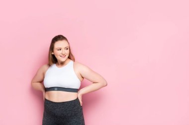 Spor kıyafetli neşeli şişman kız kalçalarına el ele tutuşup pembeye bakıyor.