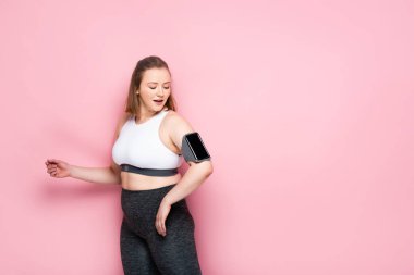 Oldukça kilolu bir kız pembe kolluk takmış akıllı telefona bakıyor.