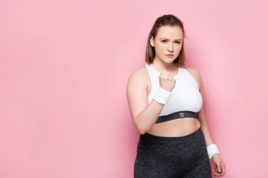 Kızgın şişman kız yumruğunu sıkar ve pembe kameraya bakar.