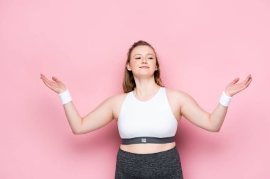 Gülümseyen şişman kız spor kıyafetleri içinde kollarını pembeye açmış duruyor.