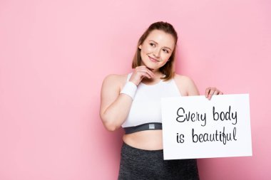smiling overweight girl holding placard with every body is beautiful inscription on pink clipart