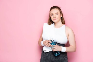 Omzunda havluyla gülümseyen şişman kız pembe şişeyle spor şişesini tutuyor.