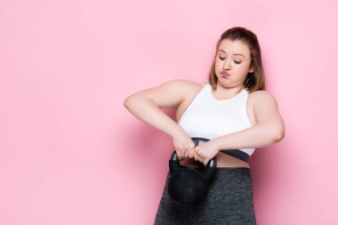 Pembe üzerine ağır bir ağırlık kaldırırken spor kıyafetleri giyen güzel ve cüsseli bir kız.