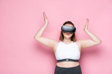 Kafası karışık bir beden artı vr kulaklıklı kız ve spor kıyafetleri pembe omuz silkme hareketi gösteriyor.
