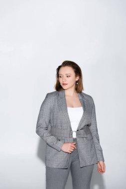Kendine güvenen, kilolu, güzel bir kız griye poz verirken gözlerini kaçırıyor.