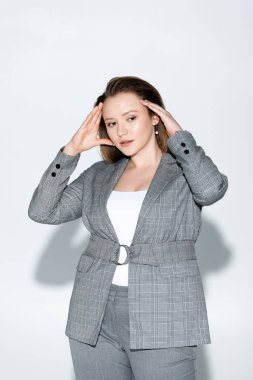 Çekici, kendine güveni tam, kilolu bir kız saçlarına dokunup gri üzerinde poz veriyor.