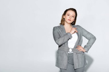 Çekici, şık, kilolu bir kız kameraya bakarken elleri kalçasında griye bakıyor.