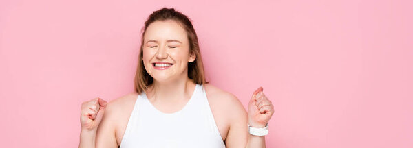 horizontal image of excited overweight girl showing winner gesture on pink