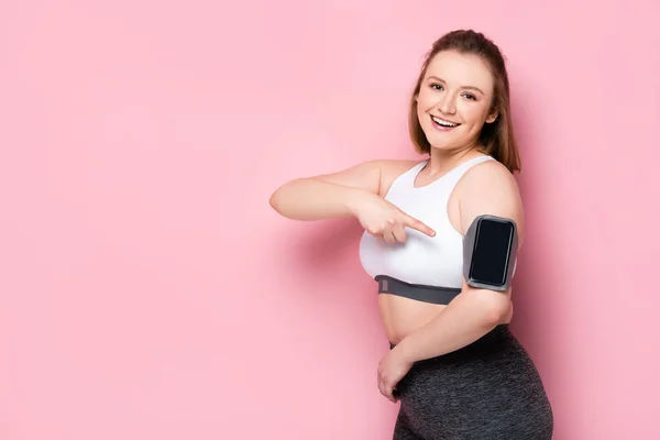 Happy Overweight Girl Menunjuk Dengan Jari Smartphone Armband Pada Pink — Stok Foto