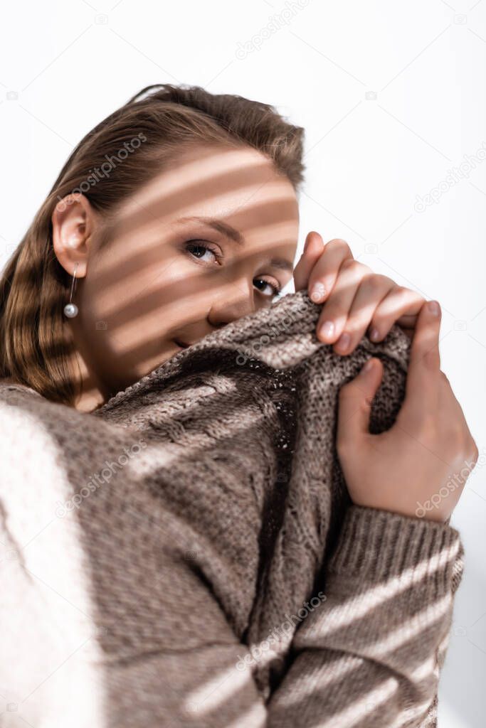 attractive overweight girl obscuring face with grey sweater and looking at camera on white with sunlight and shadows