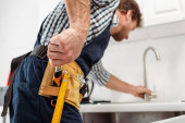 Selektiver Fokus des Klempners, der Schraubenschlüssel vom Werkzeugband nimmt, während er Wasserhahn in der Küche fixiert 
