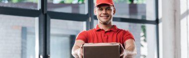 panoramic shot of happy delivery man holding carton box  clipart
