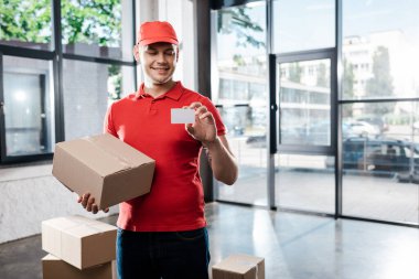 Kapüşonlu mutlu teslimatçı elinde boş kart ve karton kutu tutuyor. 