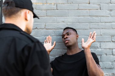 selective focus of african american man with raised hands looking at policeman, racism concept  clipart