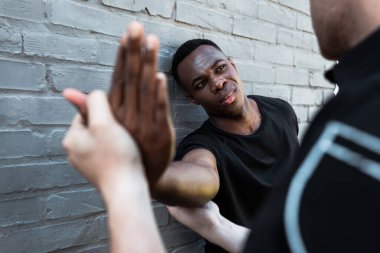 selective focus of injured african american man looking at policeman touching hand, racism concept  clipart