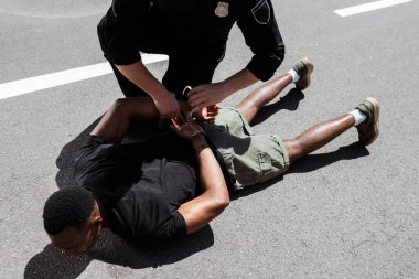 Ellerinde kelepçeler olan bir polis memuru, Afro-Amerikan bir adamı, ırkçılık konseptiyle sokakta yatarken tutukladı. 