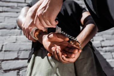 cropped view of policeman touching handcuffed african american man clipart