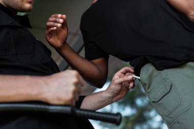 cropped view of police officer taking joint from pocket of african american man  clipart