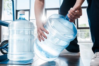 cropped view of delivery man holding blue bottle with water near hand truck  clipart