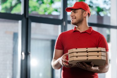 Şapkalı mutlu teslimatçı başını çeviriyor ve elinde pizza kutuları tutuyor. 