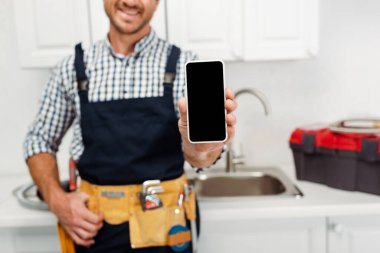 Gülümseyen işçinin seçici odak noktası mutfakta boş ekranla akıllı telefon göstermesi 