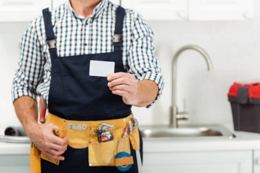 Alet kemeri takmış tesisatçı görüntüsü mutfaktaki boş kartı tutuyor. 