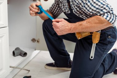 Cropped view of plumber holding insulating tape while fixing sink in kitchen  clipart