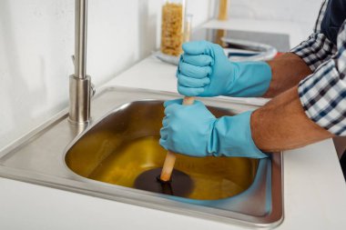 Lastik eldivenli bir tesisatçı mutfak lavabosunun tıkanmasını lavabo pompasıyla temizliyor.