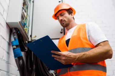 Elektrikçinin seçici odak noktası, elektrik panelinin yanında çelik yelek ve yelek tutan pano.