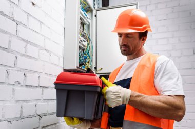 Elektrik dağıtım kutusunun yanında alet çantası tutan yakışıklı elektrikçi.