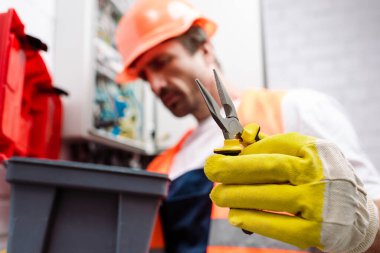 Elektrikçinin seçici odak noktası, alet çantasının yanında pense tutması. 