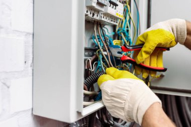 Elektrikli dağıtım kutusunu tamir ederken elinde pense tutan eldiven takan işçi görüntüsü.