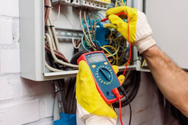 Cropped view of workman in gloves using multimeter while checking voltage of electric panel clipart