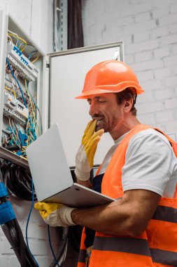 Elektrikçinin eldiveni çıkardığı ve dizüstü bilgisayarı elektrik dağıtım kutusunun yanında tuttuğu yan görüntü