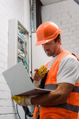 Elektrik kutusunun yanında dizüstü bilgisayarı tutan yakışıklı elektrikçi.