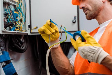 Cropped view of electrician using insulating tape while fixing wires of electric panel clipart