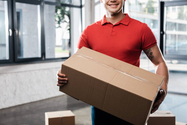 cropped view of positive delivery man holding carton box
