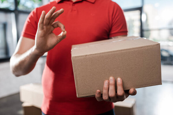 cropped view of delivery man holding carton box and showing ok sign 