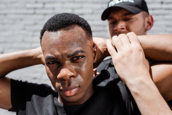 selective focus of detained african american man looking at camera near policeman 