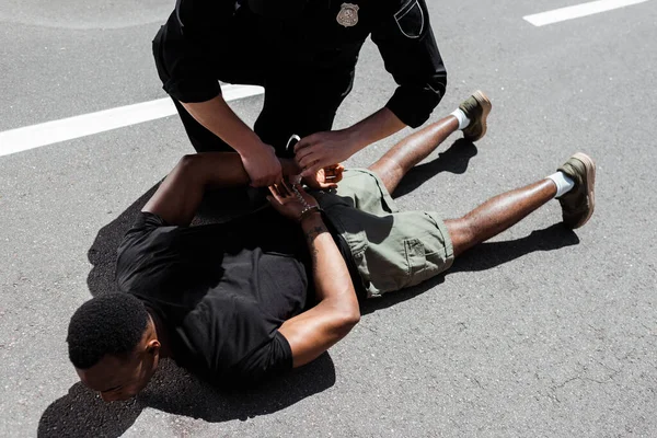 Police Officer Holding Handcuffs While Detaining African American Man Lying — Stock Photo, Image