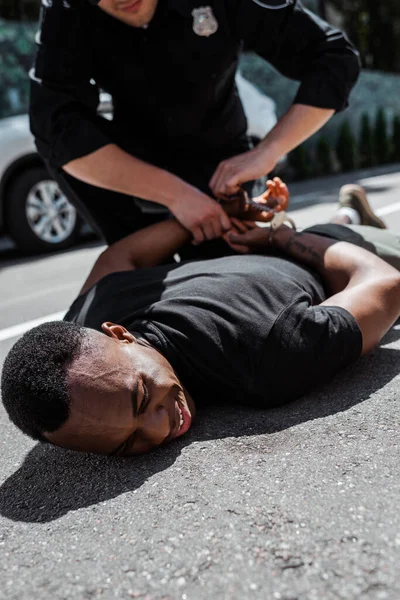Tutuklanan Afrikalı Amerikalı adamın seçici odak noktası kelepçeli ve ırkçılık kavramı ile polisin yanında yerde yatması. 