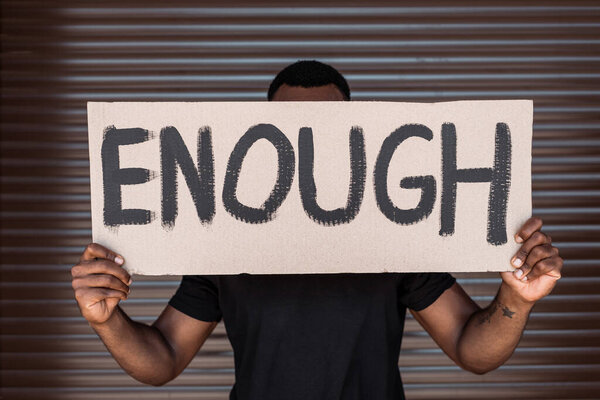 african american man covering face while holding placard with enough lettering on street, racism concept 