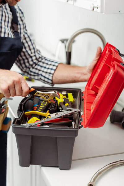 Обрезанный вид водопроводчика с гаечным ключом на кухонном столе
 