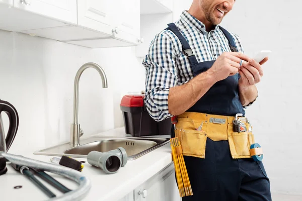 Vista Cortada Encanador Sorridente Usando Smartphones Perto Ferramentas Bancada Cozinha — Fotografia de Stock