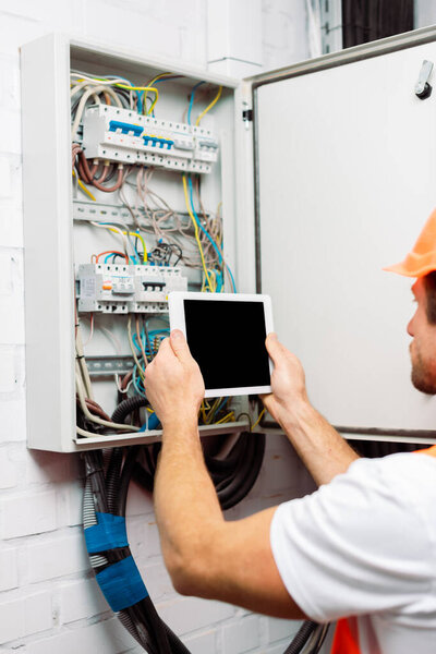 Selective focus of electrician holding digital tablet with blank screen near electric panel