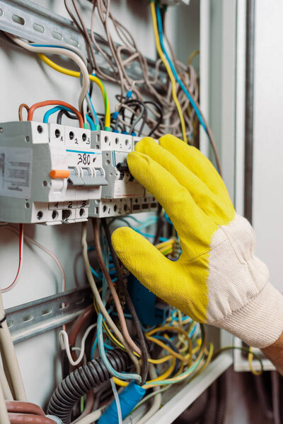 Cropped view of electrician in glove including toggle switches of electric panel