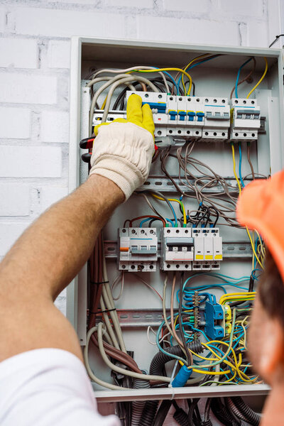 Selective focus of electrician in glove holding pliers and turning on toggle switches of electrical box