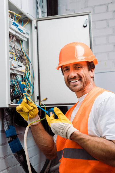 Smiling electrician holding insulating tape and wires while fixing electric panel