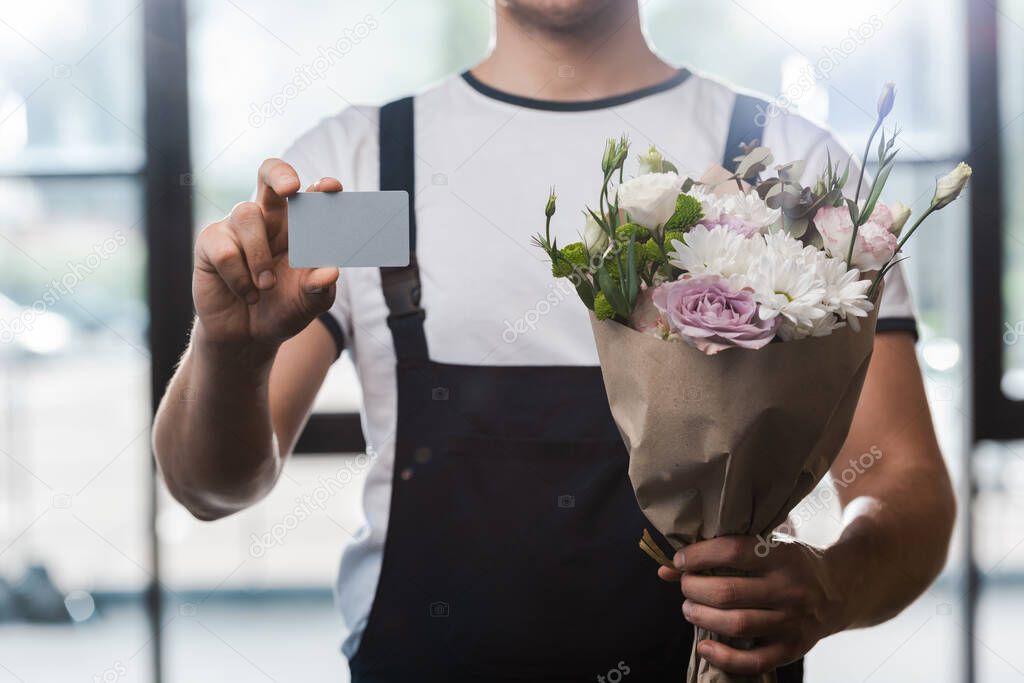 cropped view of delivery man holding bouquet with flowers and blank card 